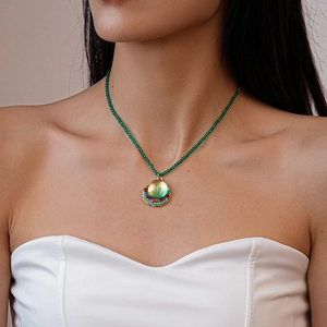 Detail of green beaded necklace with colorful round pendant worn on a female model