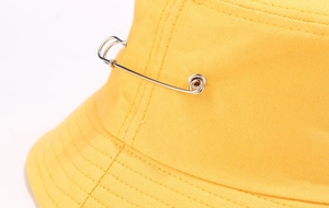 Détail rapproché d'un bob en coton jaune avec une épingle de sûreté décorative en argent