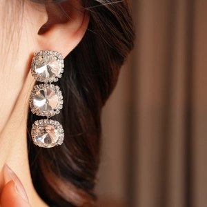 Close-up of sparkling silver tassel earrings with round diamond clusters on a model