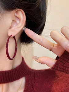 Close-up of elegant burgundy enamel hoop earrings on model with matching sweater