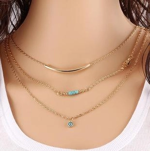 Detail of layered gold necklace featuring a curved tube, turquoise beads, and Evil Eye charm