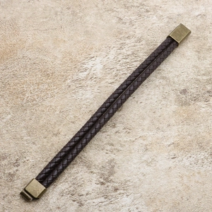 Braided dark brown leather bracelet with vintage brass alloy clasp on beige background