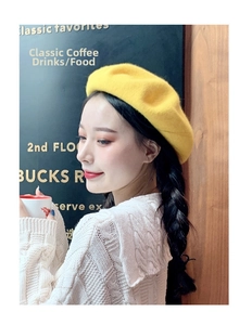 Detail of a bright yellow wool beret hat worn by a model in a cozy cafe setting