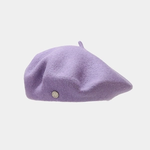 Detailed texture of dark purple wool beret featuring a vintage metal logo badge