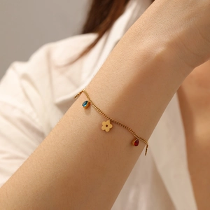 Detail of gold chain bracelet with blue and red gemstone drops and flower charm