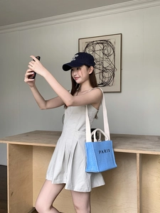 Blue straw tote bag with PARIS lettering styled with beige dress and navy cap