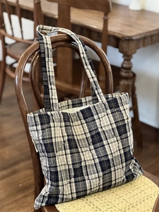 Detail of blue and white quilted plaid cotton tote bag resting on a vintage wooden chair