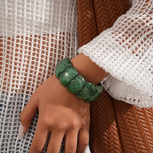 Close-up of a chunky green acrylic bracelet with glittering sequins on a model wrist