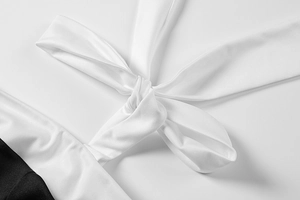 Detail of white tie-up ribbon on a black and white pleated A-line dress with knit texture