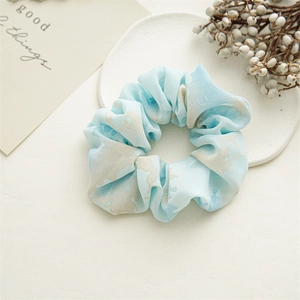 Detailed close-up of a light blue floral scrunchie on a white decorative display tray