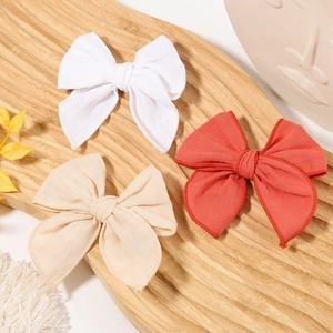 Three cotton linen bow hair clips in white, beige, and red on a rustic wooden tray