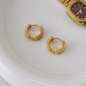 Dettaglio di orecchini a cerchio intrecciati placcati oro 18K su vassoio bianco