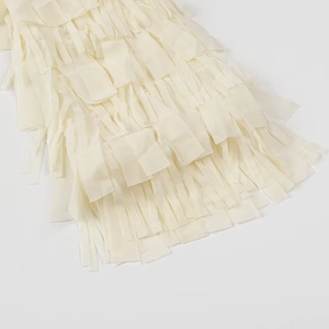 Close-up of beige fringe layers and flowy fabric detail on the long sleeve shirt