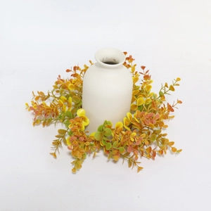 Top view of yellow and orange eucalyptus candle ring surrounding a white ceramic vase