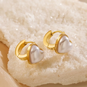 Elegant gold heart pearl earrings on a stone display with a soft warm aesthetic