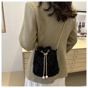 Detail of black quilted denim bucket bag featuring frayed edges and white pearl charms