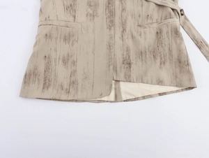 Dettaglio dell'orlo del gilet beige con trama effetto legno scuro e cinturino con bottone