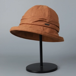 Detailed side view of a brown linen bucket hat featuring a small metal brand logo plaque