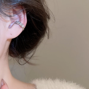 Gros plan d'un ear cuff argenté serti de zircons porté sur le cartilage de l'oreille