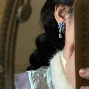 Detail of floral tassel earring with blue petals and teardrop pendant on a model