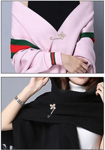 Detail of a gold clover brooch pin with sparkling rhinestones on a sweater and scarf