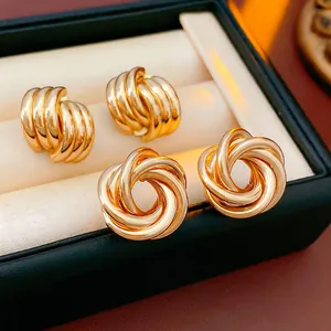Golden geometric spiral earrings and twisted knot studs set on white velvet liner