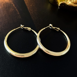 Close-up of polished golden geometric hoop earrings with secure clasp on black background