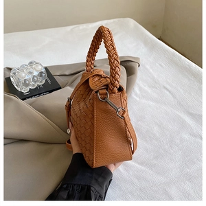 Detail shot of brown woven leather handbag with thick braided handle and metal hardware