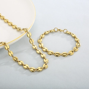 Close-up of golden coffee bean link necklace and bracelet set on a white ceramic plate