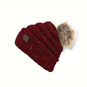 Détail d'un bonnet en tricot bordeaux chiné avec un pompon en fausse fourrure douce