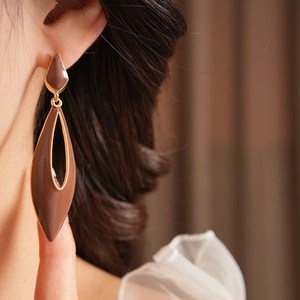 Close-up of vintage brown enamel teardrop earring with gold trim on model ear