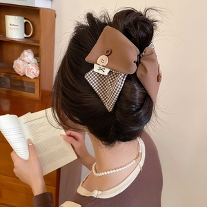 Close-up of brown checkered bow hair clip with button detail on model in cozy setting