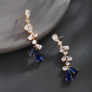 Macro detail of gold-plated drop earrings featuring blue and clear teardrop crystals