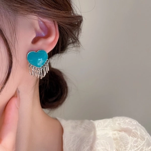 Detailed close-up of a silver tassel earring with a glossy teal heart-shaped stud