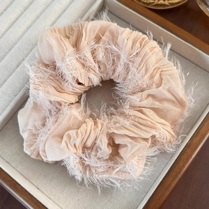 Macro shot of beige fabric scrunchie with fringe edges on a jewelry tray detail
