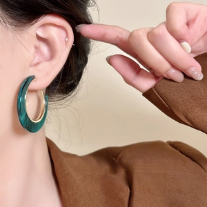 Detail of green acrylic and gold geometric hoop earrings worn by a model in close-up