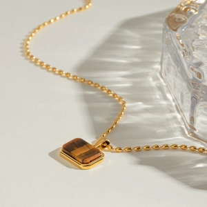 Macro shot of tiger eye stone pendant on 18k gold bead chain against wavy glass light