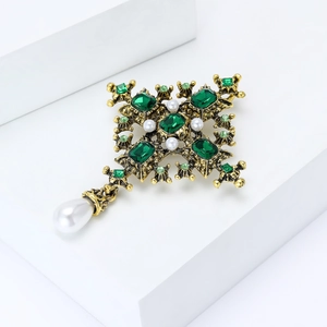 Baroque cross brooch with green gems and teardrop pearl on a white display stand
