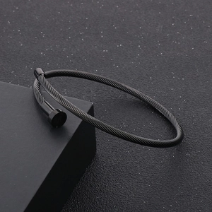 Macro detail of black cable twist bangle with screw cap accents on dark textured stand