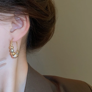 Close-up of a gold hoop earring with varied metallic beads worn with a brown blazer
