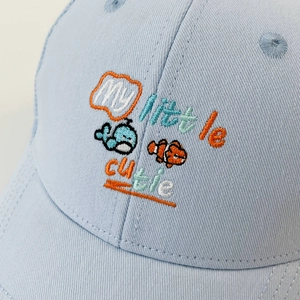 Close-up of baby baseball cap with blue whale embroidery and my little cutie text