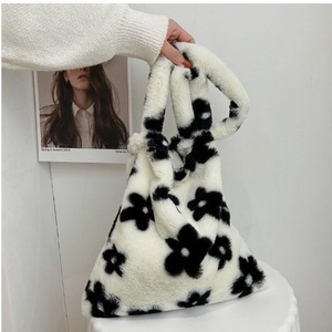 Detailed view of white plush tote bag with black floral patterns on a white table
