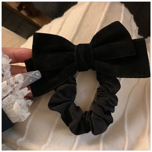 Detail of a black velvet bow hair tie held by a hand in elegant white lace gloves