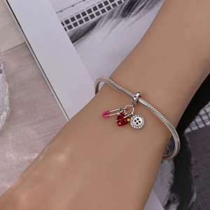 Detail of silver snake chain bracelet featuring pink enamel pin and red heart charms