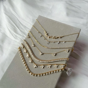 Close-up of golden olive leaf fringe necklaces and tennis chains on grey velvet