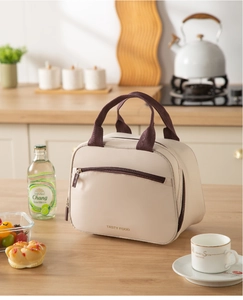 Detail of beige insulated lunch bag showing front zipper pocket and gold logo print