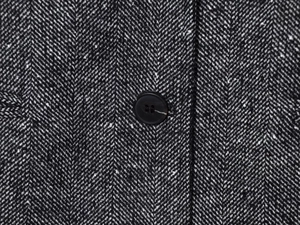 Macro di tessuto tweed a spina di pesce grigio con bottone nero sulla giacca lunga