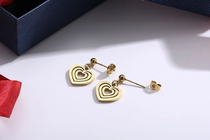 Detail view of golden multi-layer heart stud earrings placed on a blue gift box