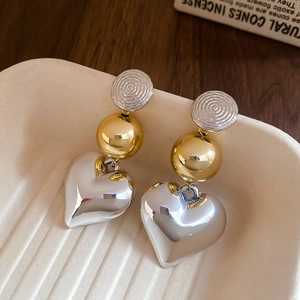 Macro shot of long silver heart drop earrings with gold bead detail in a textured tray