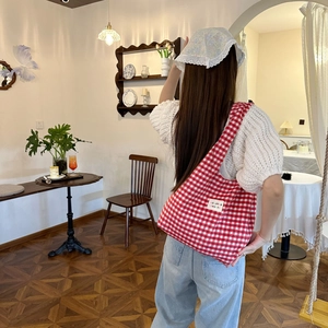 Detail der rot-weiß karierten Stoff-Tragetasche kombiniert mit Strickoberteil und Jeans